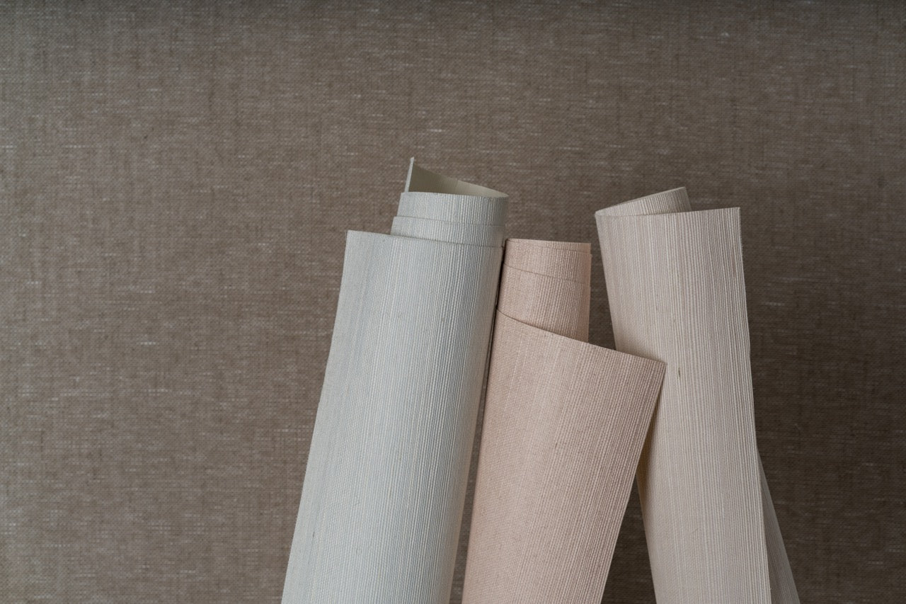 Three pastel colored rolls of grasscloth shown in front of a tan background