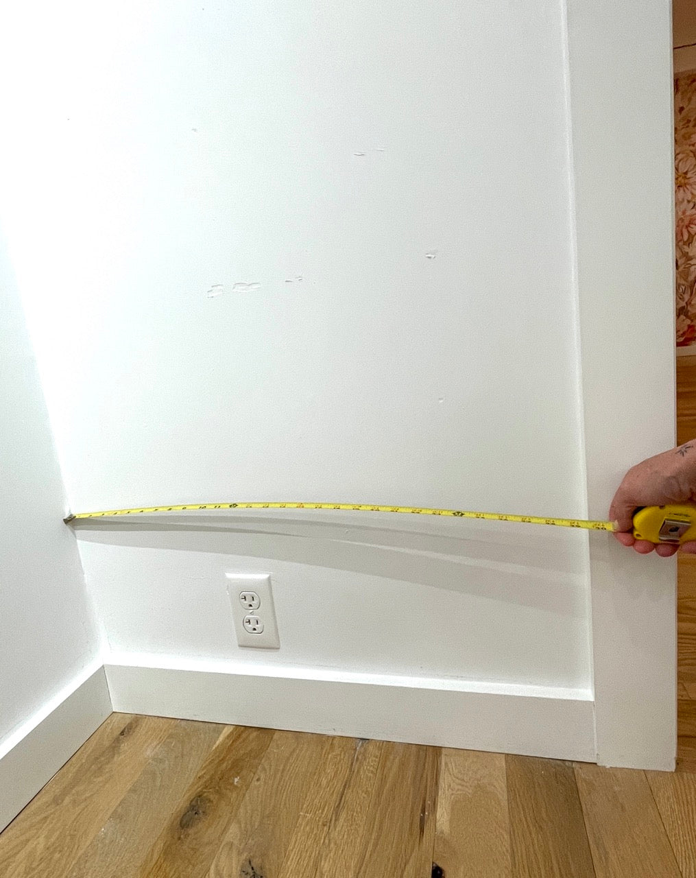 Hand with a tape measure against a white wall to show how to measure wall width for wallpaper