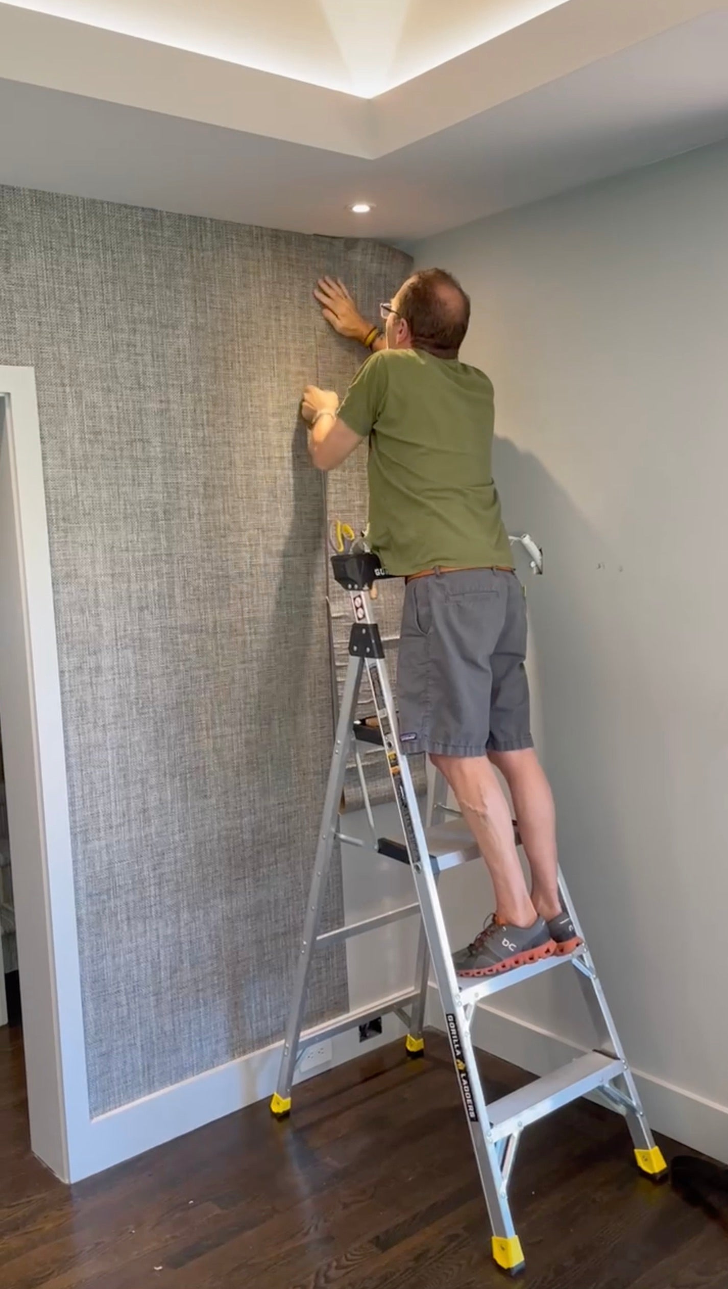 A man standing on a ladder hanging grasscloth wallpaper