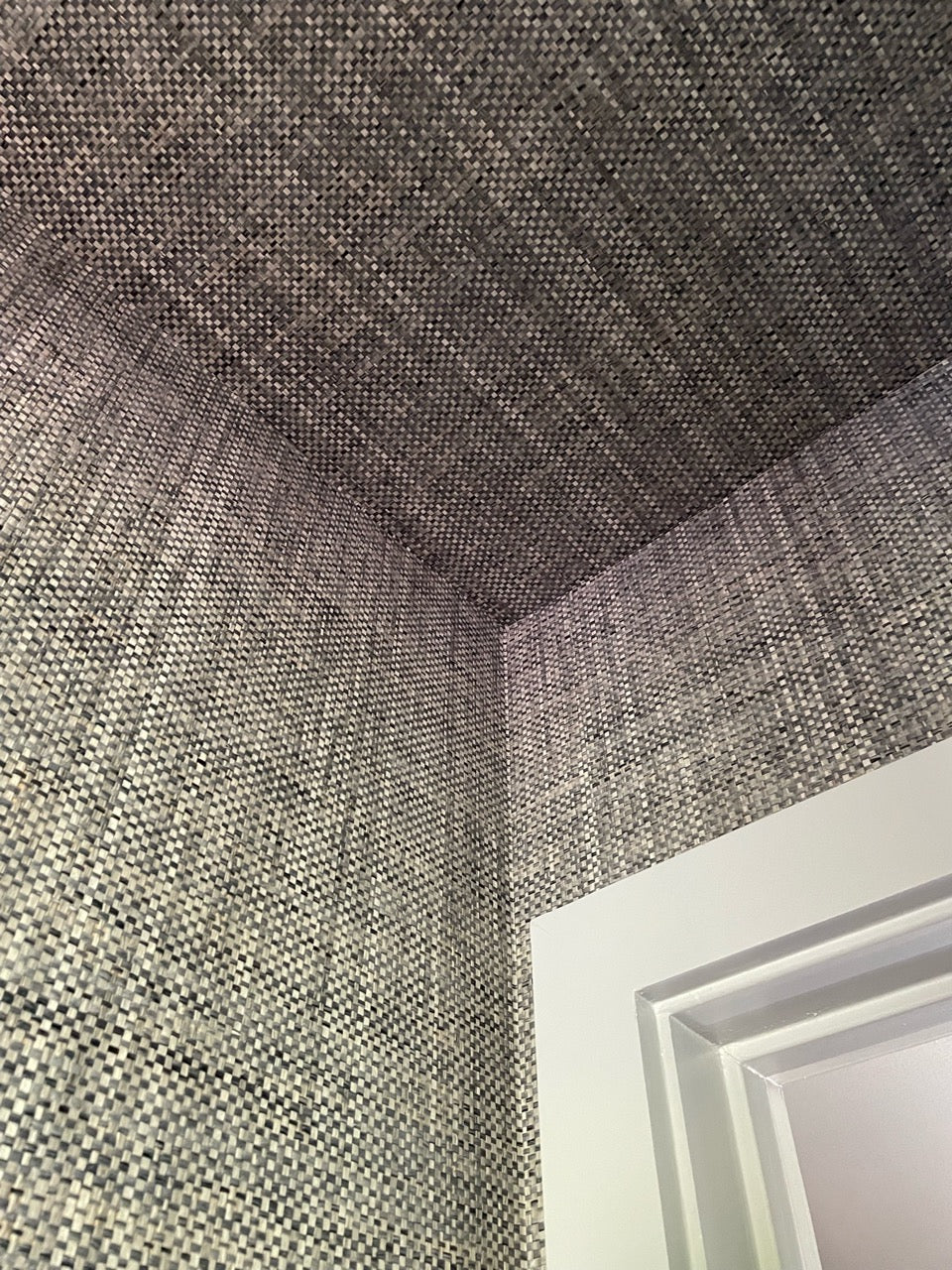 Two walls and the ceiling meet covered in paperweave grasscloth wallpaper