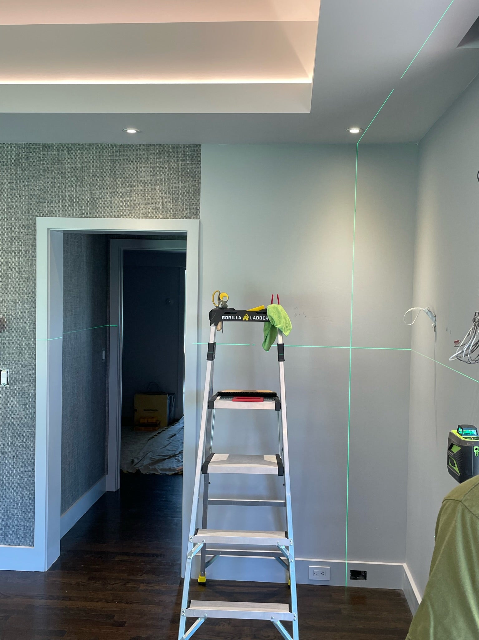 Inside a room facing a wall with green laser lines for placing wallpaper and a ladder