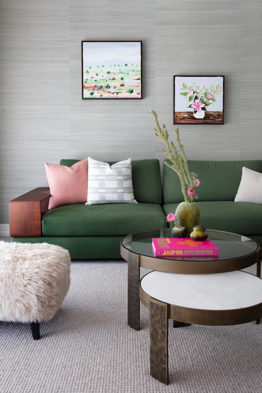 A green sofa with pink and white pillows against a wall of light gray grasscloth