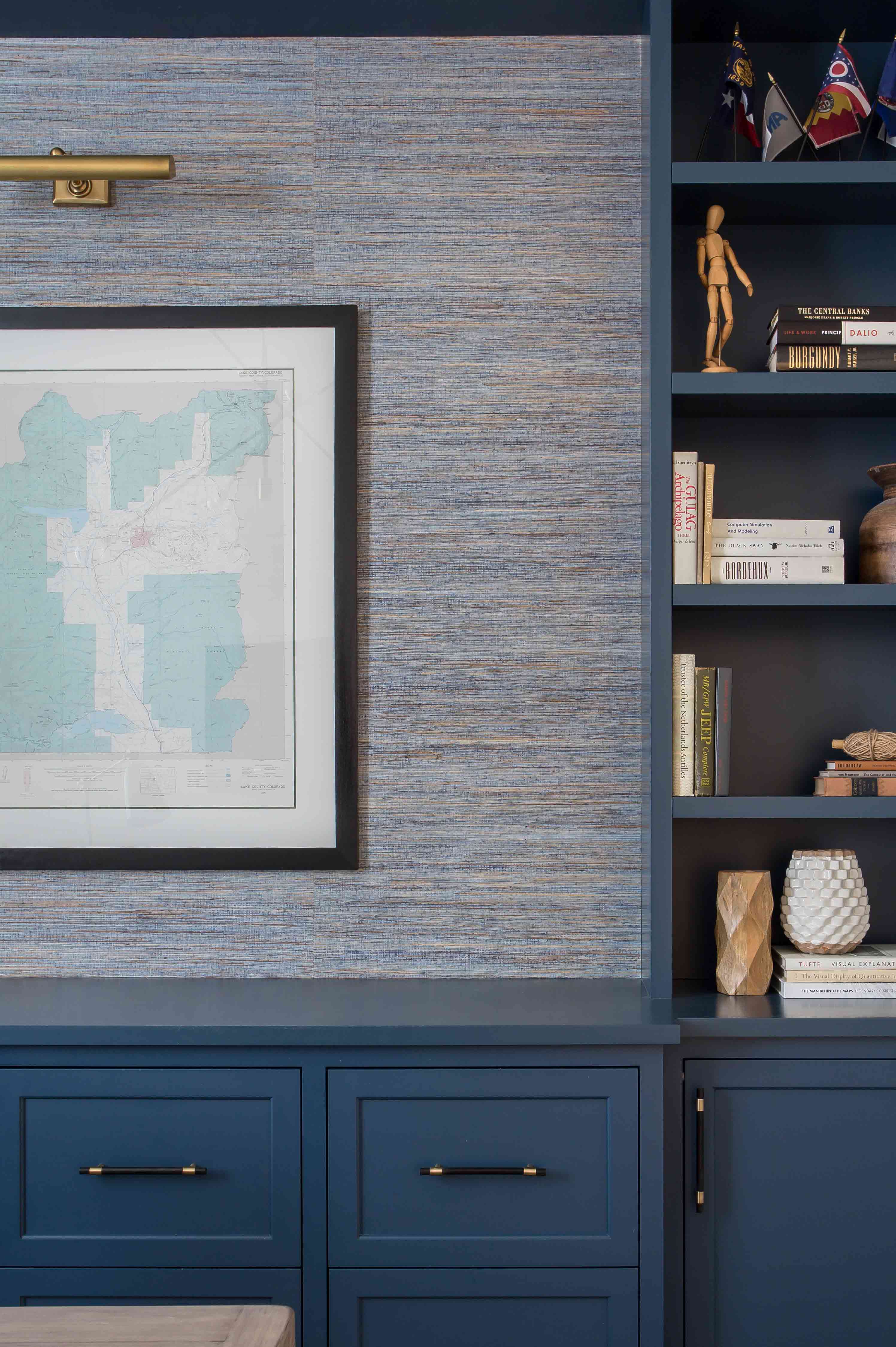 Light blue textured grasscloth wall with framed old map and cadet-blue bookshelf nearby.