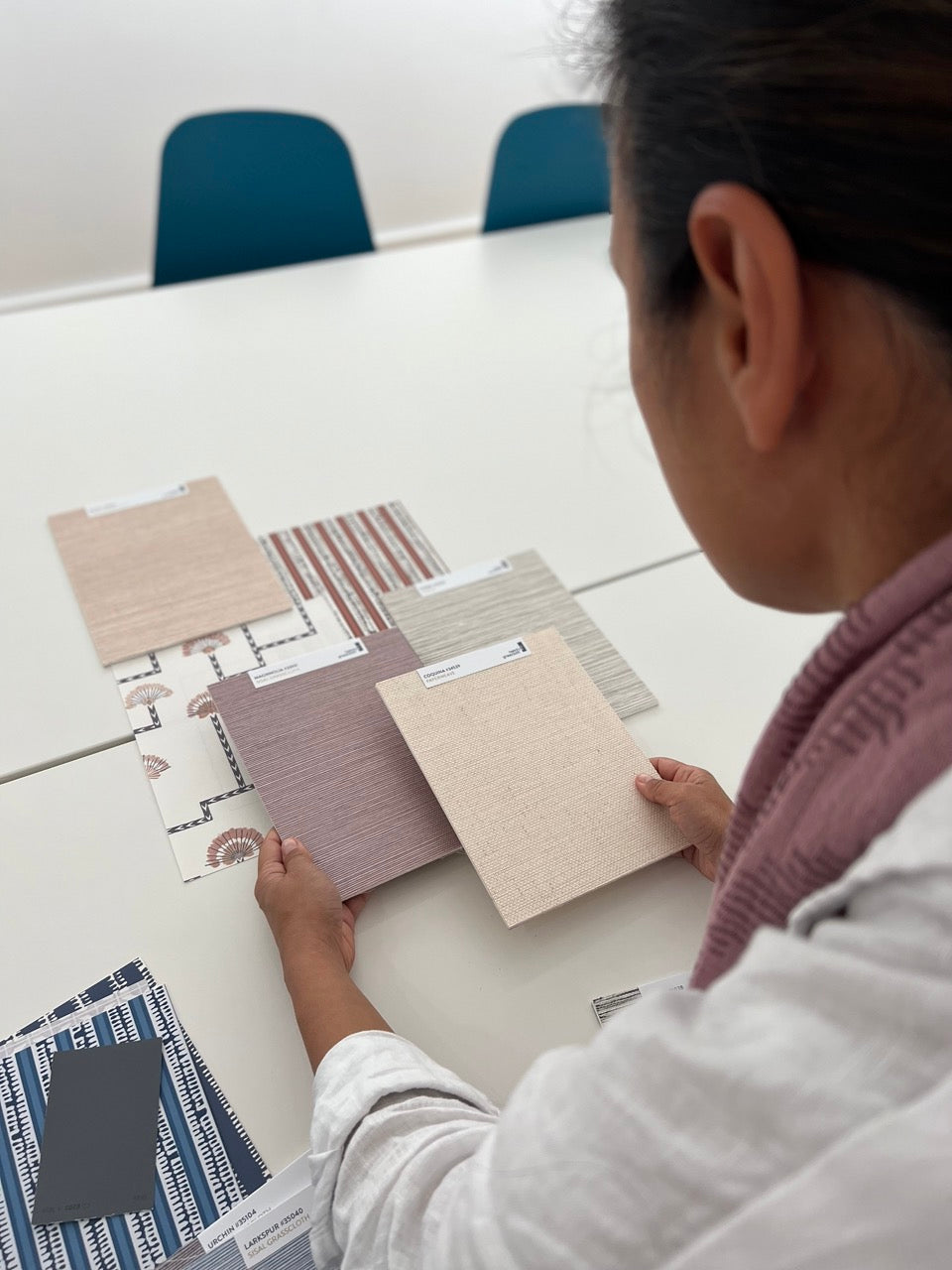 A person seated at a white table evaluating different spring decor grasscloth swatches laid out in front of them.