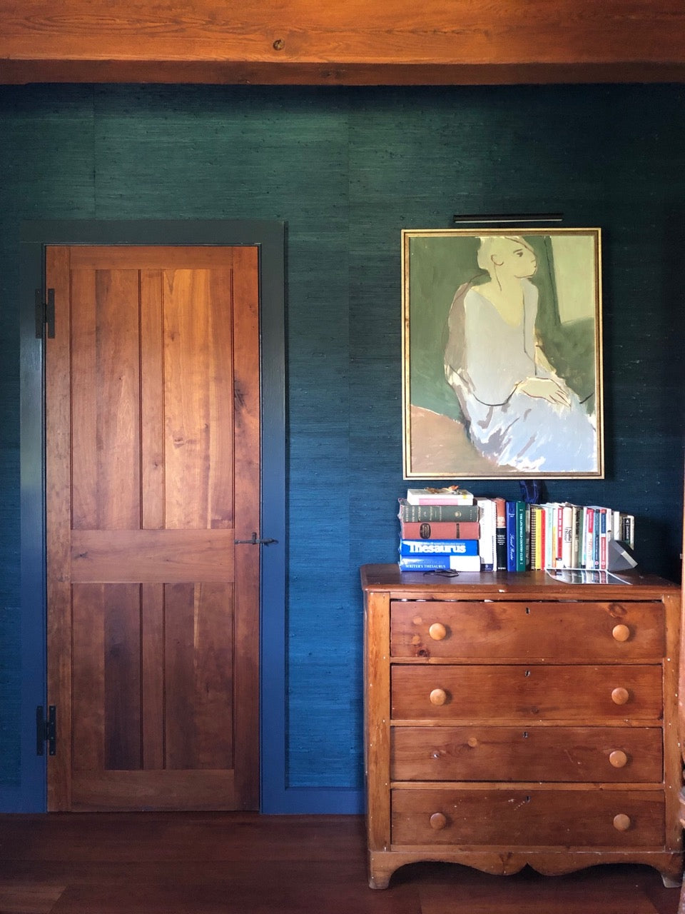 Close up of a wooden bedroom door and dresser with navy blue grasscloth wallpaper