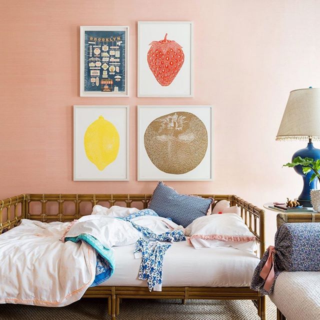 Unmade daybed in front of a wall of artwork with pink grasscloth wallpaper