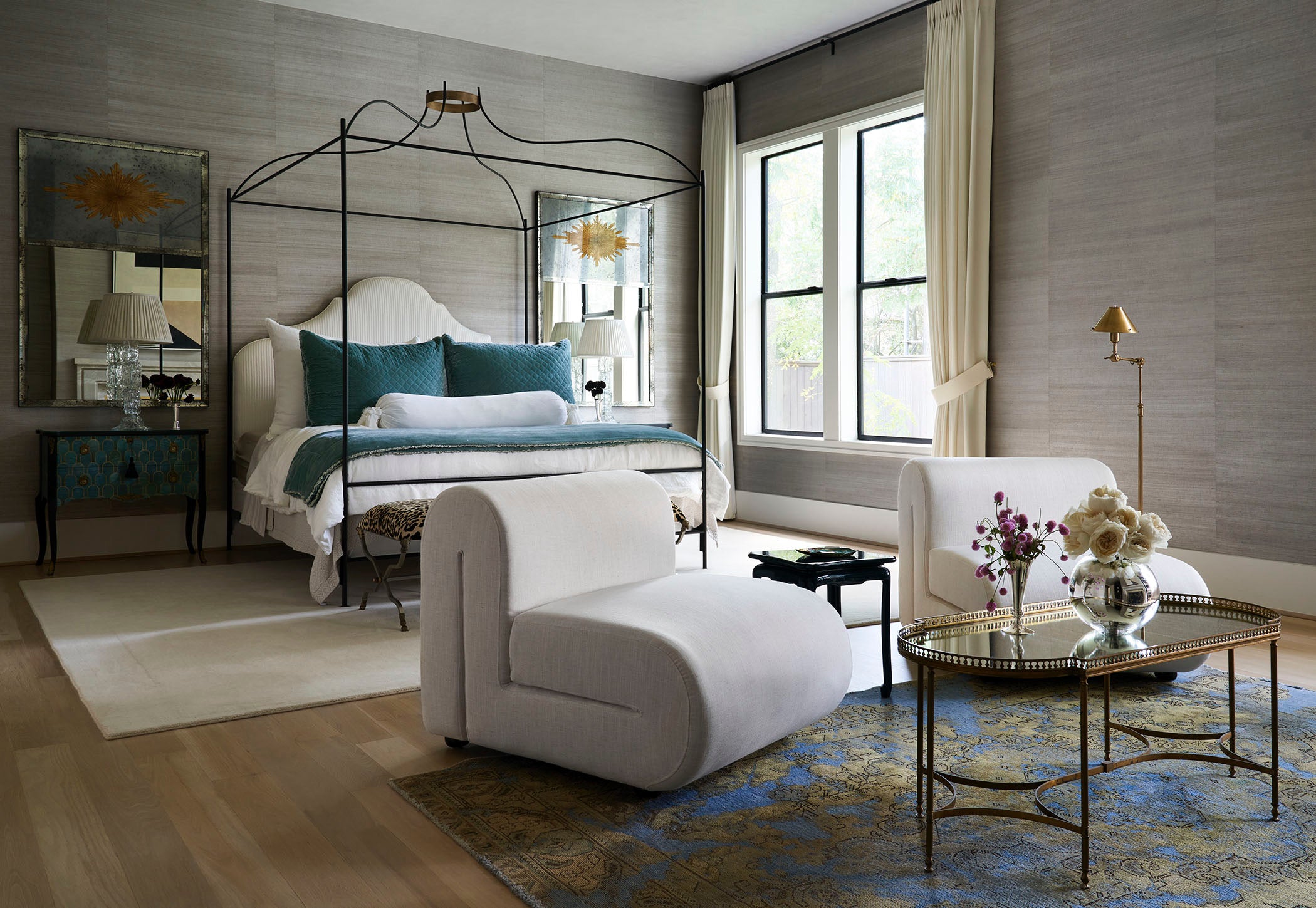 Large bedroom with four poster bed, lounge chair and side table with walls covered in gray sisal grasscloth wallpaper
