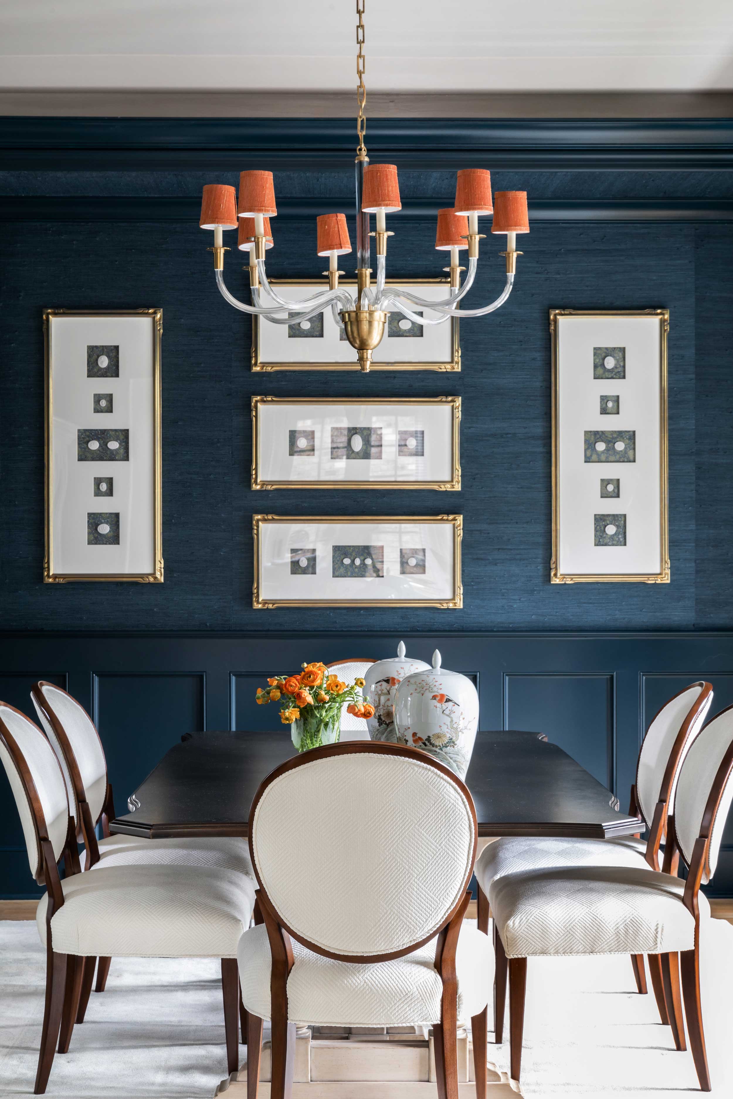 Traditional formal dining room with table and white cushioned chairs, a chandelier with orange lamp shades and a wall covered in blue grasscloth wallpaper