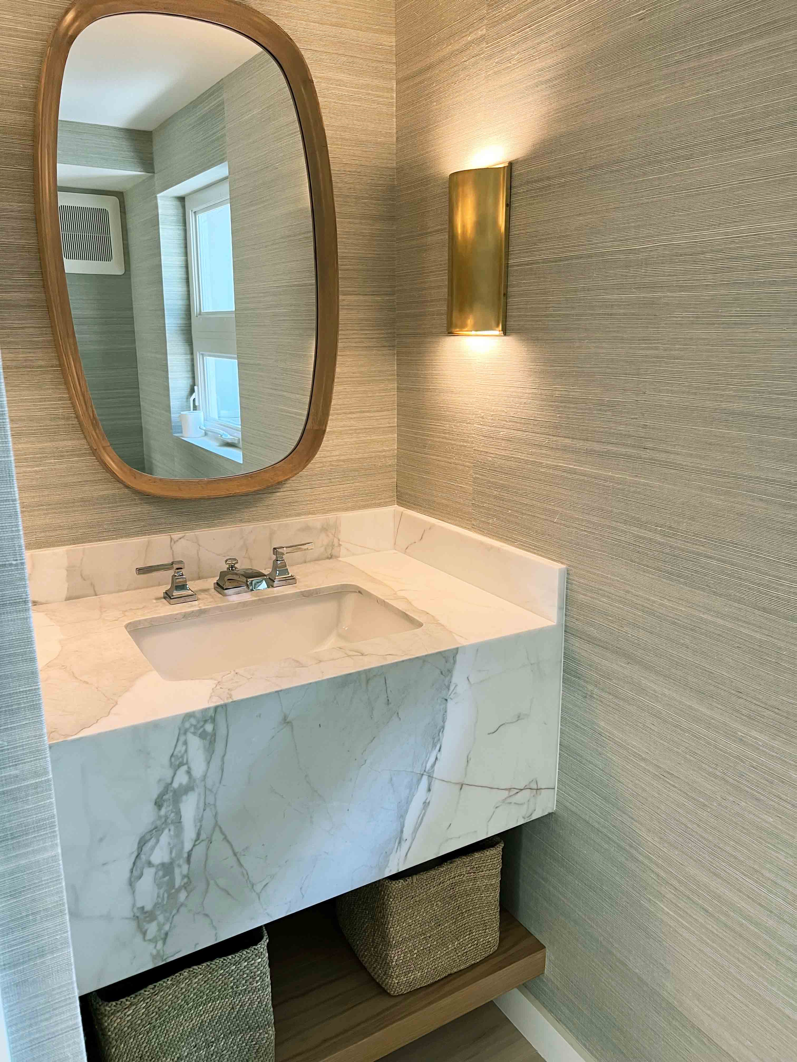 Powder room with round bronze mirror, marble sink and green grasscloth wallpaper