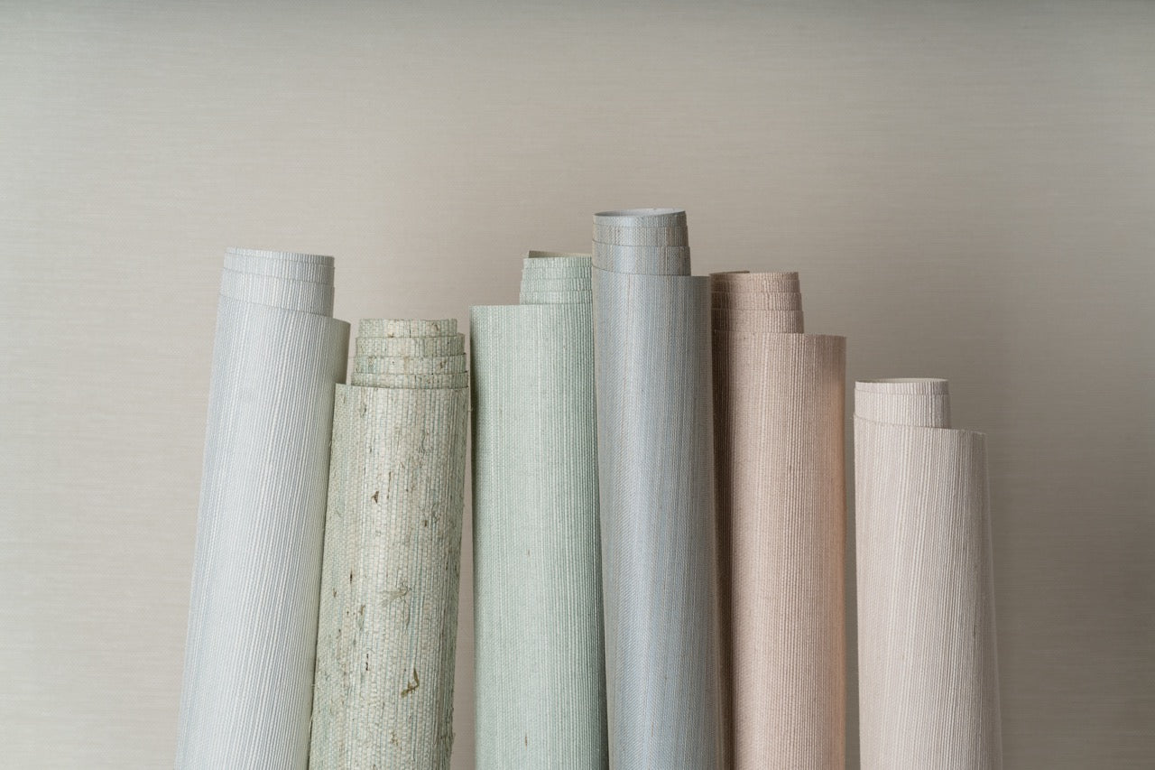 A collection of wallpaper rolls in various textures and pastel colors, ideal for spring interior design, standing upright against a light beige background.