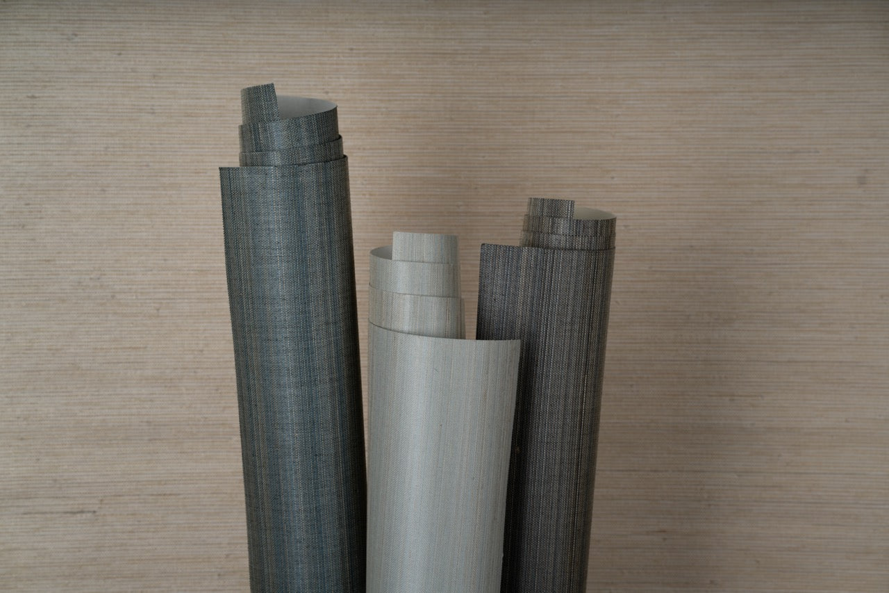 Three vertical rolls of blue, light blue, and black abaca grasscloth against a beige background.