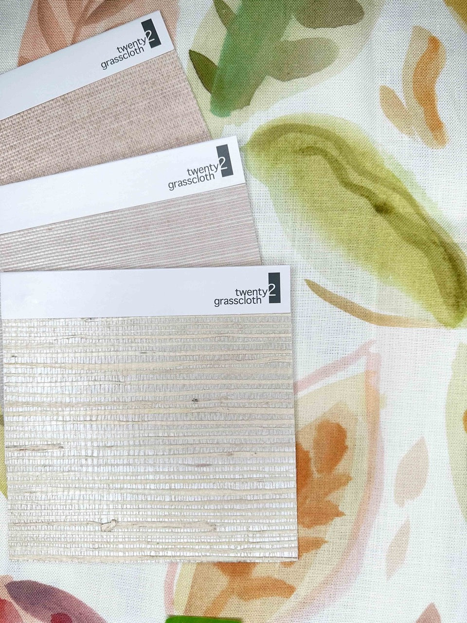 Grasscloth swatches from the "twenty2 grasscloth" collection in earthy tones on a floral print background, perfect for spring interior design.