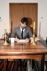 Dylan seated at a table writing wearing a gray suit.