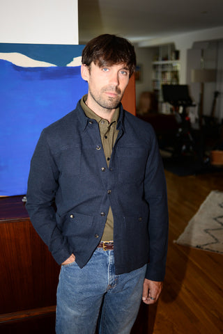 Dylan wears a green button down with a navy wool shirt jacket and jeans.