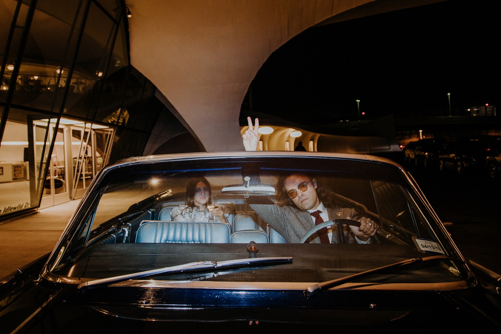 Image of wedding guests sitting in a parked convertible next to the TWA Hotel.
