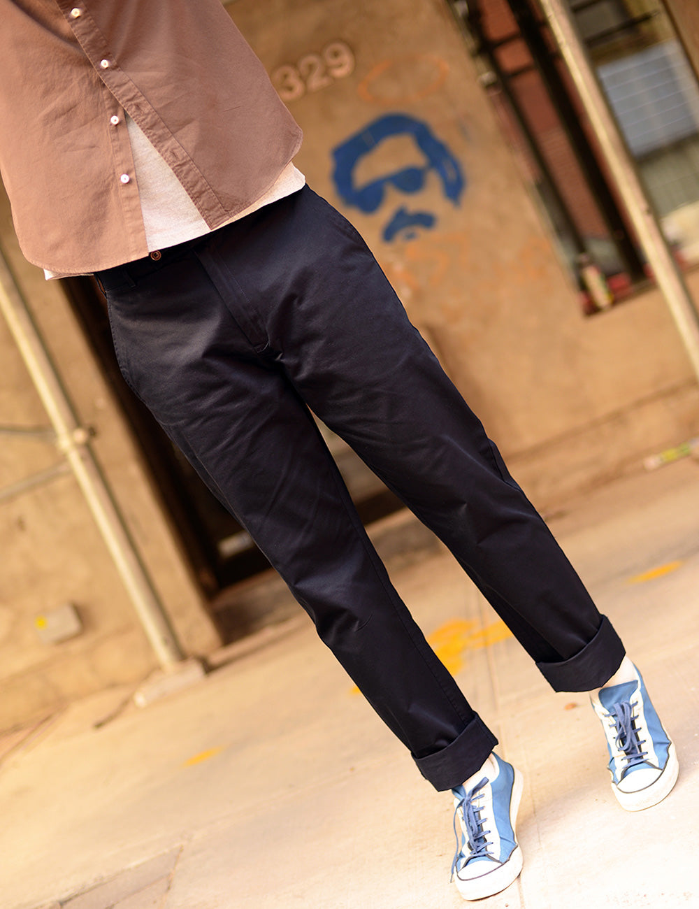 Cropped image of a model (face cropped) wearing navy chinos, sneakers, a t-shirt and an overshirt.