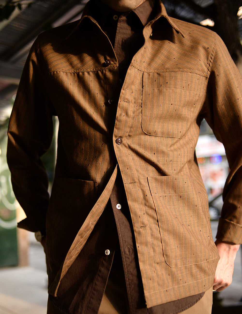 Close-up image of a model wearing a brown button down shirt with a tan shirt jacket worn over.