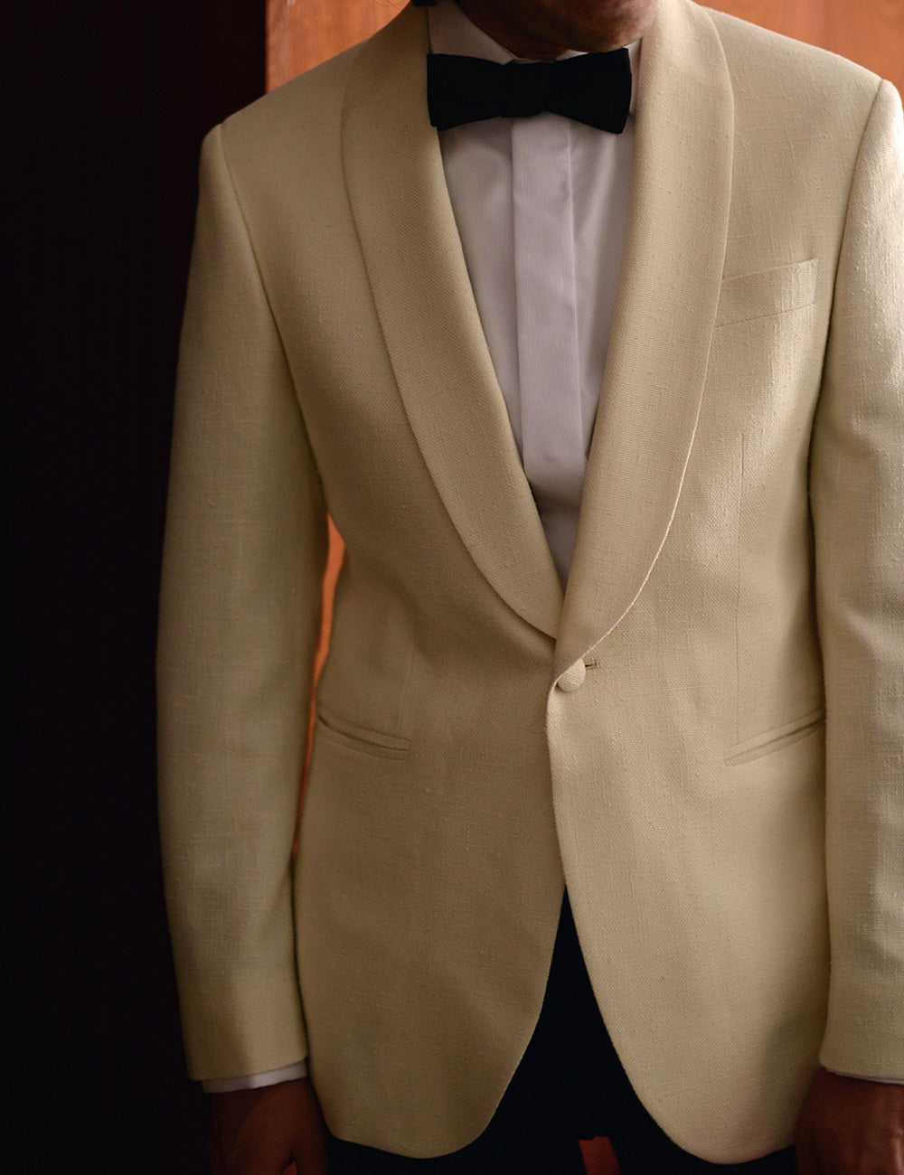 Cropped image of model wearing an ivory dinner jacket, with a white tuxedo shirt and black bow tie.