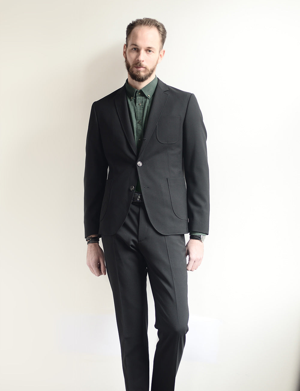 Model wears black casual suit with green button down shirt.