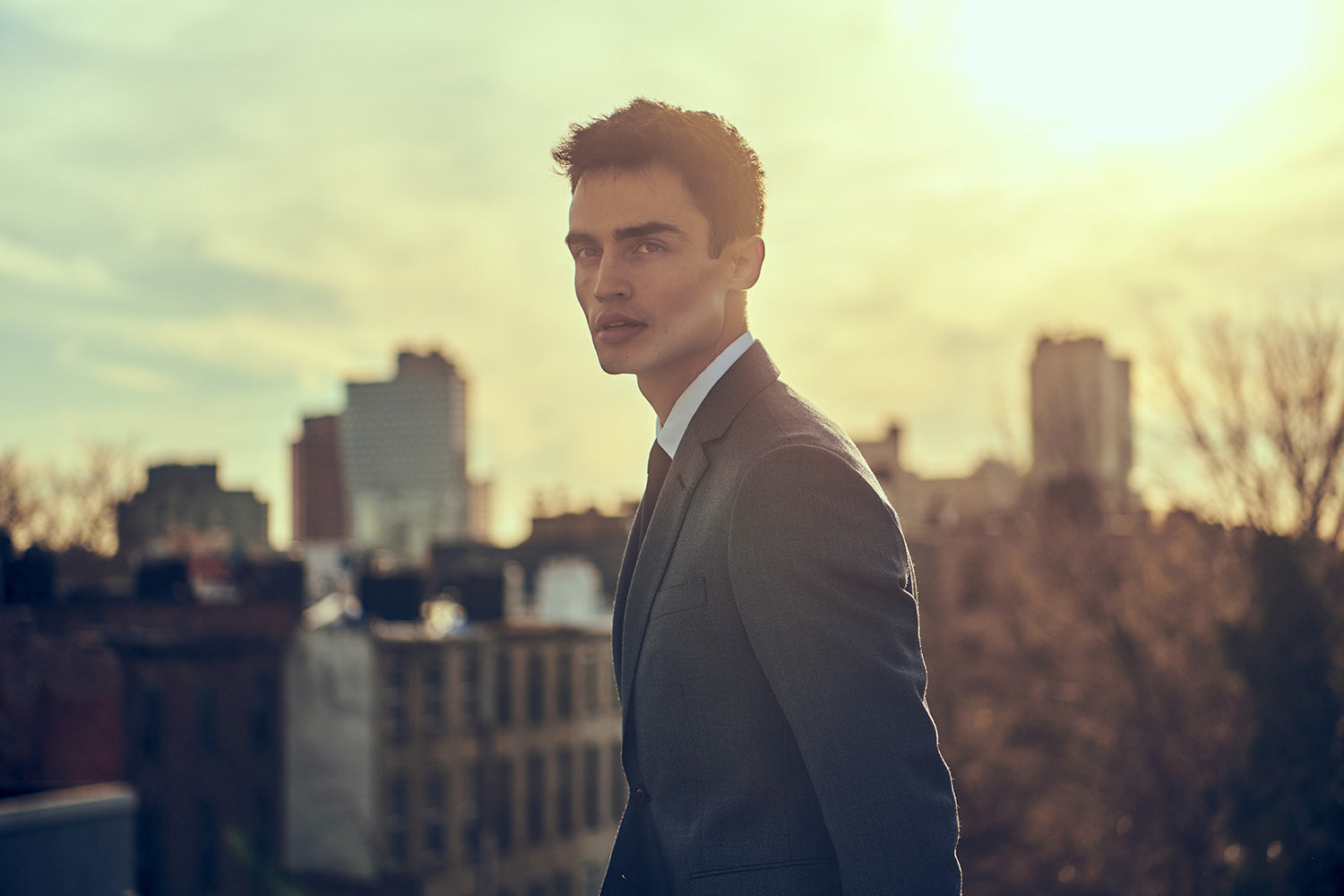 Model in light gray suit jacket, white shirt, and black tie on a NYC rooftop.