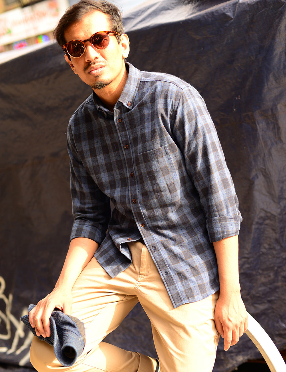 Model wears khaki chinos, a plaid flannel button down shirt and sunglasses.