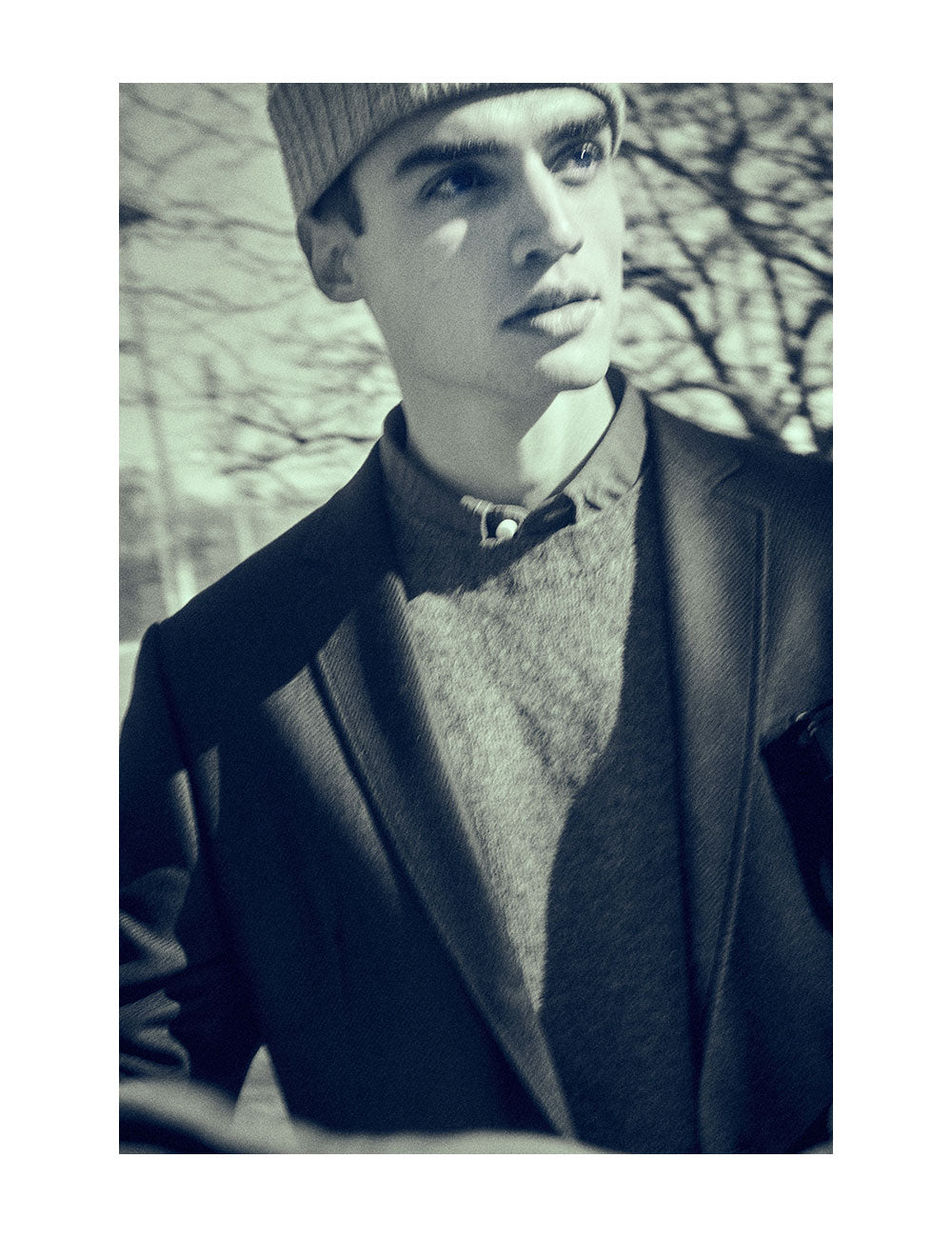 Black and white image of model wearing an unstructured blazer with a sweater and button down shirt underneath. He is also wearing a beanie.