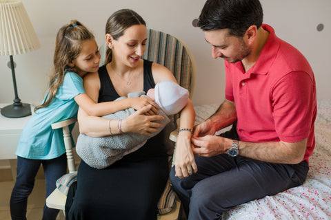 Family with newborn baby, daughter, mother and dad putting bracelet on