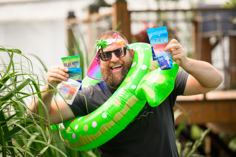 Jesse, owner of Appalachian Standard wearing tropical beach attire and holding up bags of CBD gummies