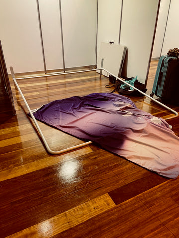 An aluminium frame on the ground and fabric draped over it, ready to be stretched over the frame and stand at the back of the booth