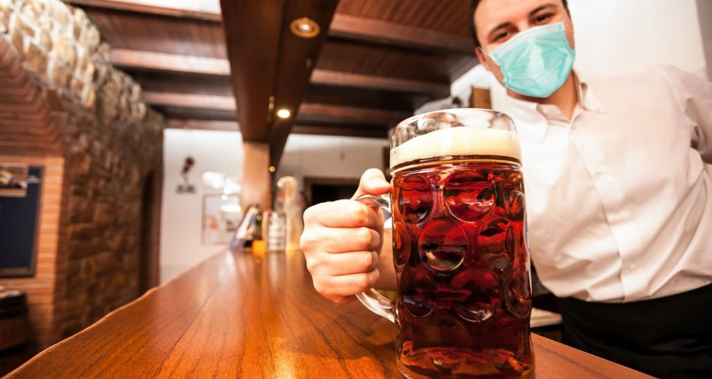 Barkeeper mit Maske hält eine Biermaß in der Hand