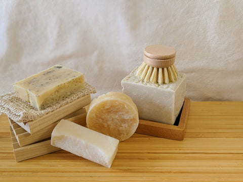 LEMON POPPYSEED BAR SOAP ON A SISAL SOAP BAG AND BOARDWALK WOODEN SOAP DISHES, A NATURALSTAIN-REMOVER STICK, ALOE + TE TREE SHAMPOO BAR, AND SOLID DISH SOAP WITH SCRUB BRUSH AND DELUXE WOODEN SOAP DISH. BAMBOO AND NATURAL COTTON BACKGROUND.