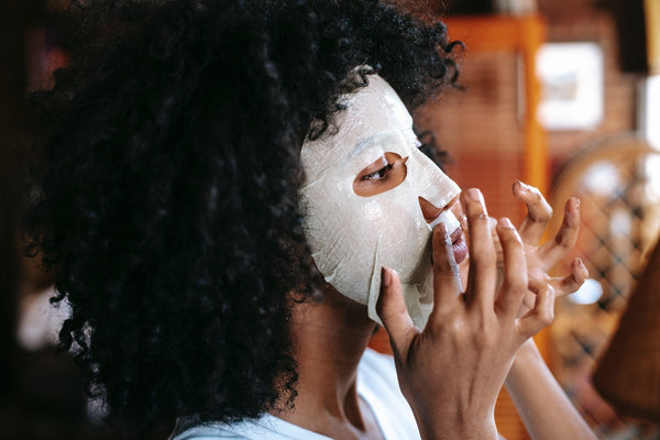 en kvinna applicerar en sheetmask för glow i ansiktet