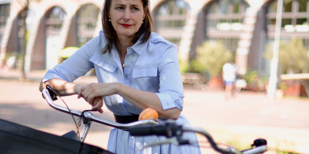 Frau in hellblauem Hemdblusenkleid hinter Fahrrad