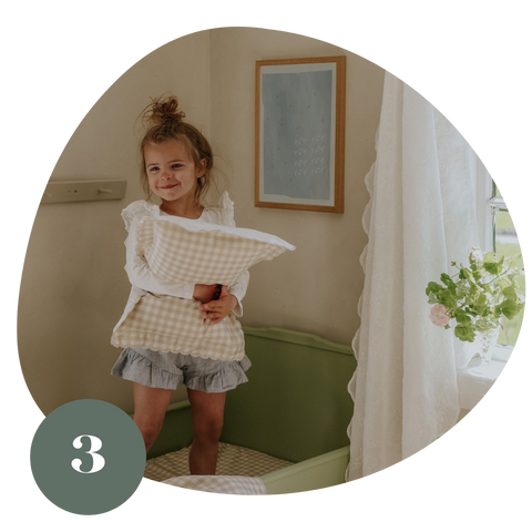 Toddler girl holding a beige gingham printed pillow