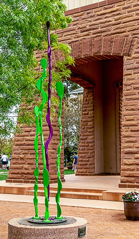 Visioning #4 green and purple hand forged sculpture on display in a public courtyard.