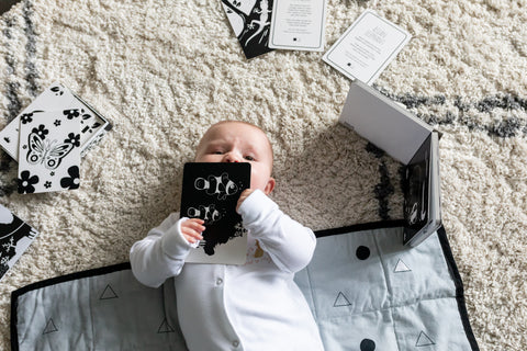 baby playing with a high contrast black and white flash card on a play mat