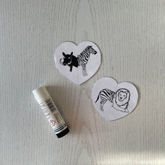 Two cut out paper hearts with animals on them next to a glue stick