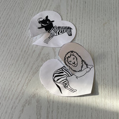 two paper hearts that have slots cut halfway down each one with black and white animals on them