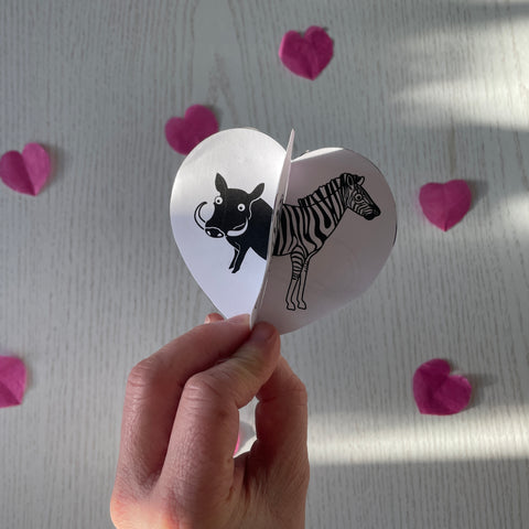 3D valentines heart craft with illustrations of warthog and zebra and pink paper hearts in the background from the little black and white book project