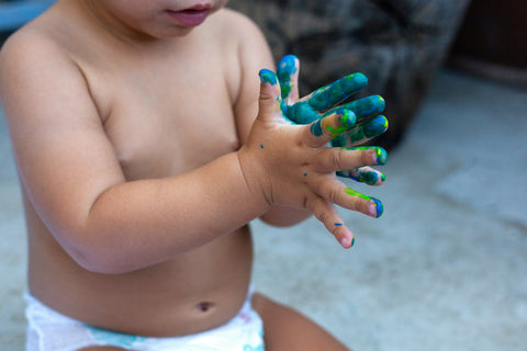 close up of baby in a nappy with paint on their hands making art