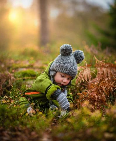 baby in bobble hat sat on woodland floor in sunlight