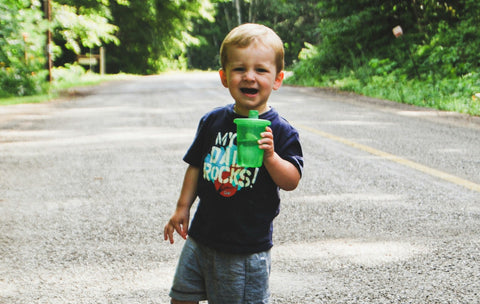 Young boy holding a green sippy cup standing in the road