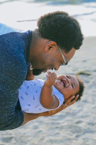father holding giggling baby on a beach