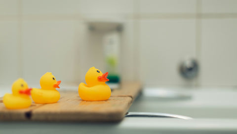 close up of 3 rubber ducks on side of a bath tub