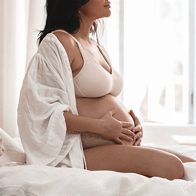 Woman gently cradles her pregnant belly, wearing Triumph Amour Maternity Bra