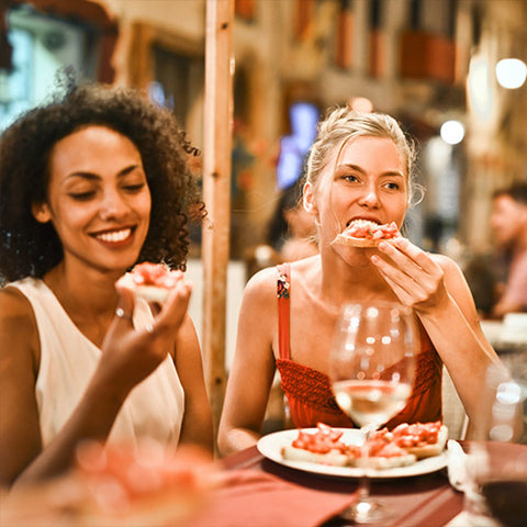 Two women eating pizza and drinking wine at restaurant