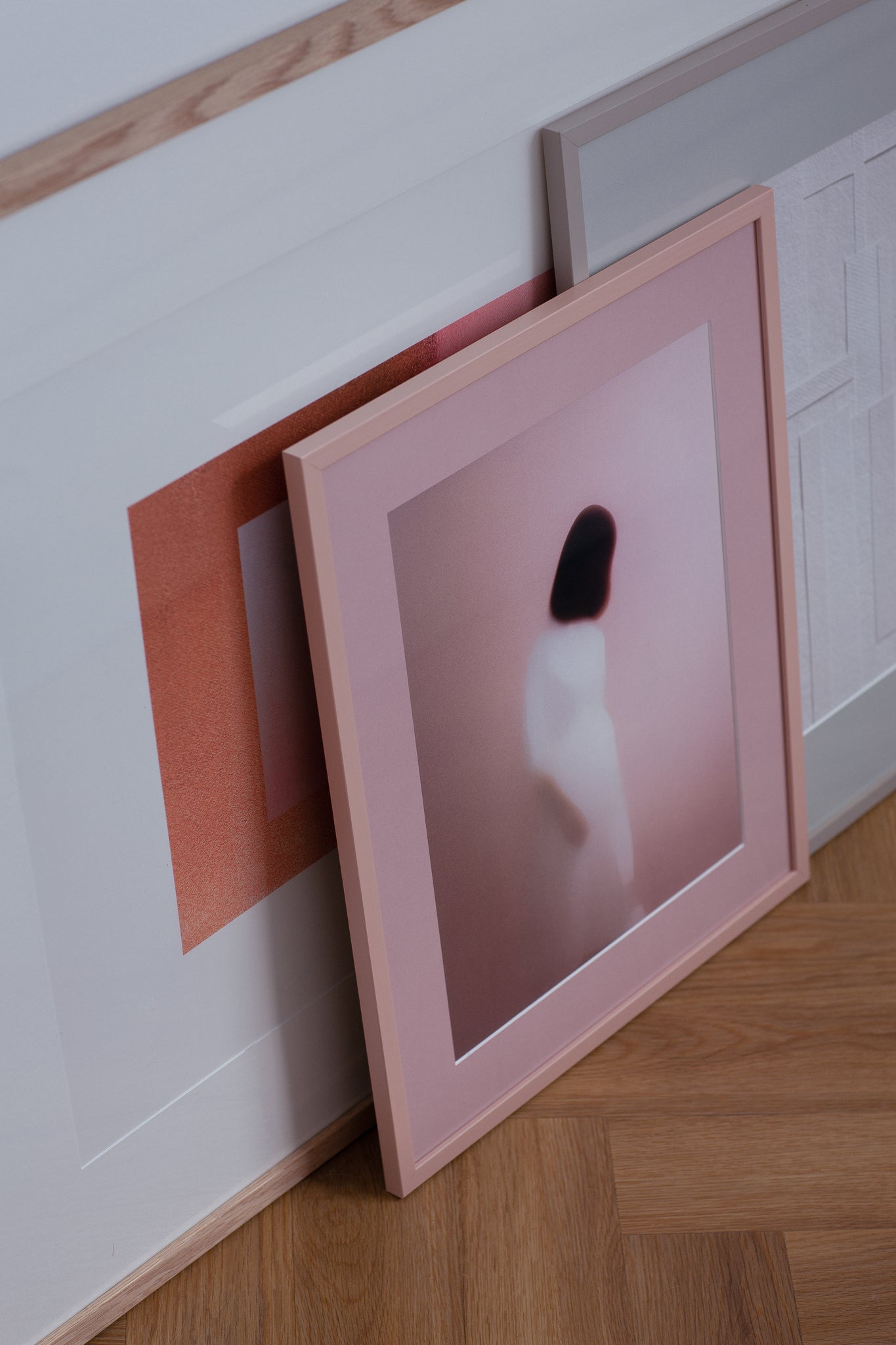 Framed abstract photography with pink and white passepartout layers resting on parquet flooring