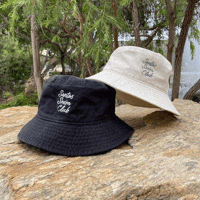 Two unstructured bucket hats in ivory and black with script embroidery Santos Swim Club