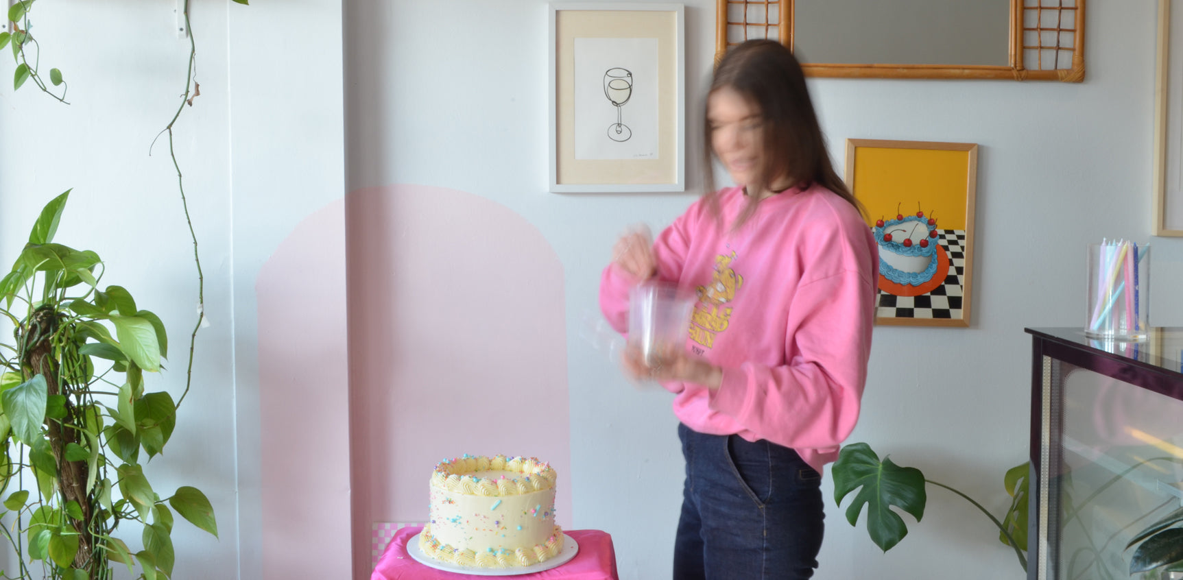 Matilda Chambers wears a pink jumper and blue jeans as she decorates a cream cake in front of her with sprinkles.