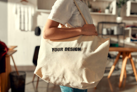 Woman holding a tote bag with YOUR DESIGN across it